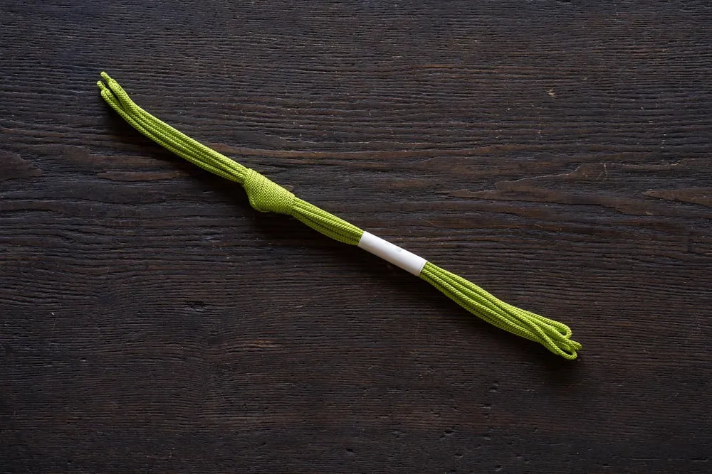 A moss-green twisted silk cord with a knot, lying on a dark wooden surface