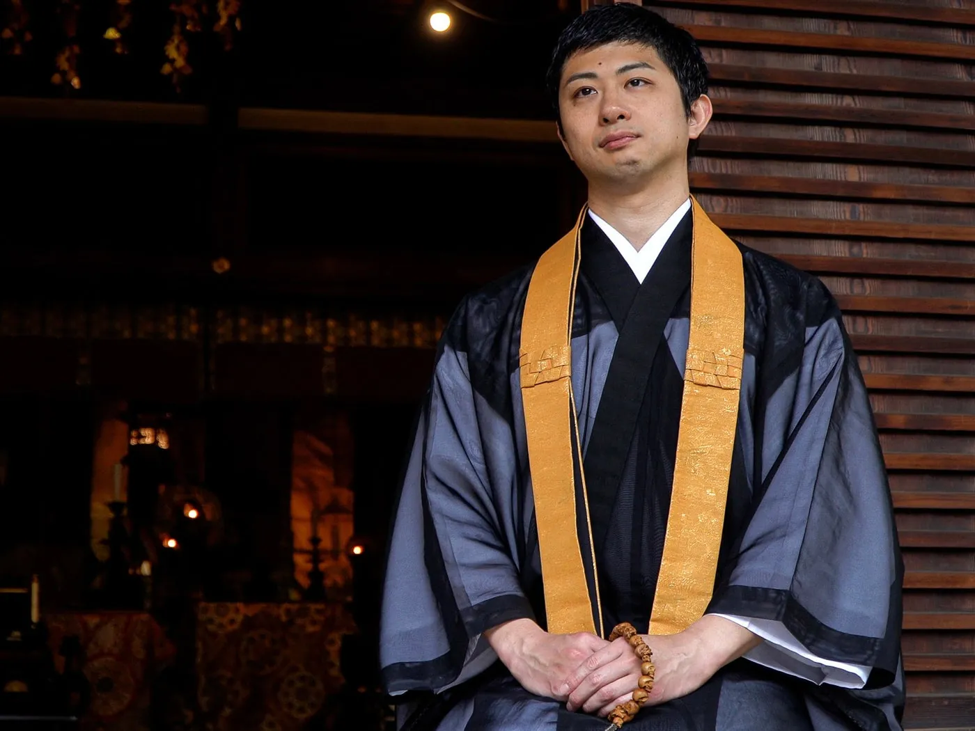 A Buddhist priest in a grey sheer robe wearing a gold-orange wagesa