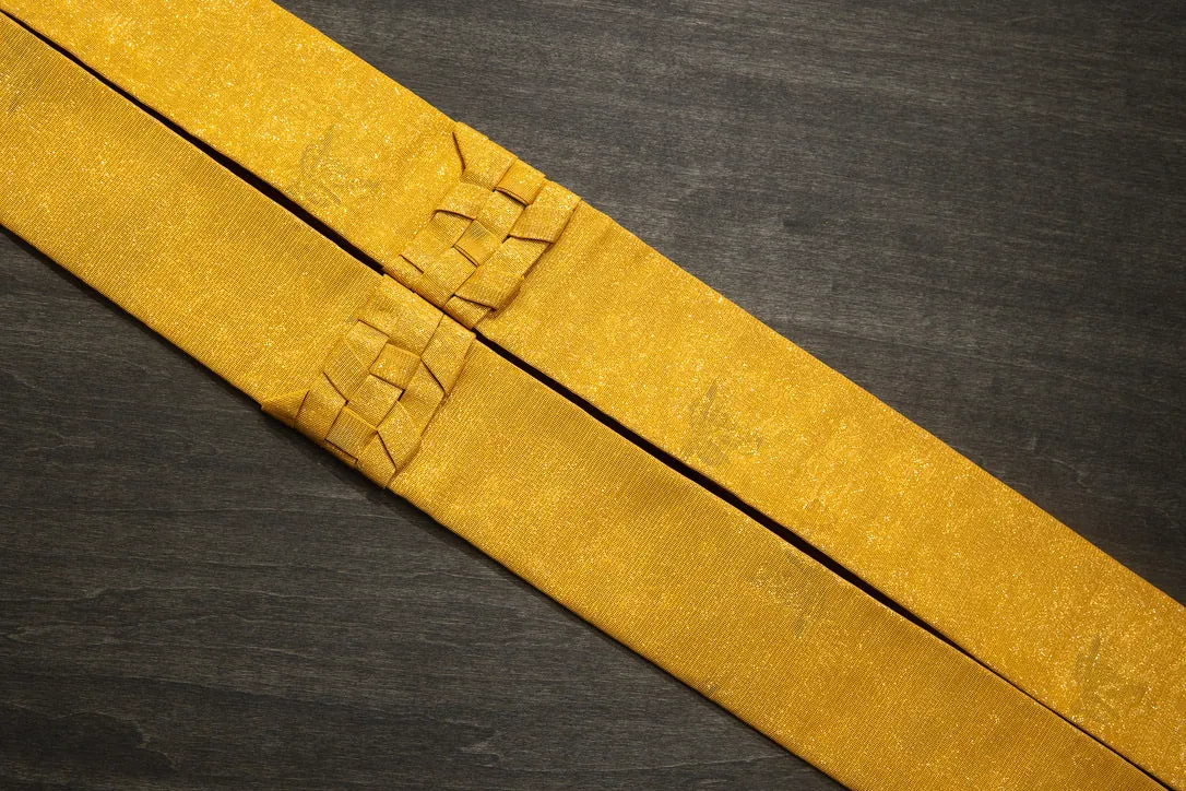A yellow-gold washable wagesa lying on dark wood, with the folded concertina section at its centre